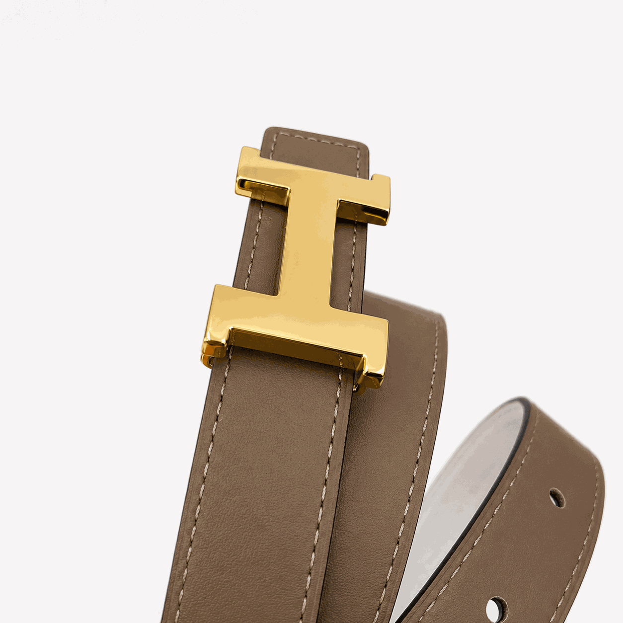 Gold H-style buckle on taupe leather belt close-up